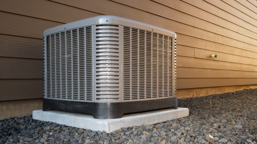 Central air conditioner condenser on a gravel pad beside a home