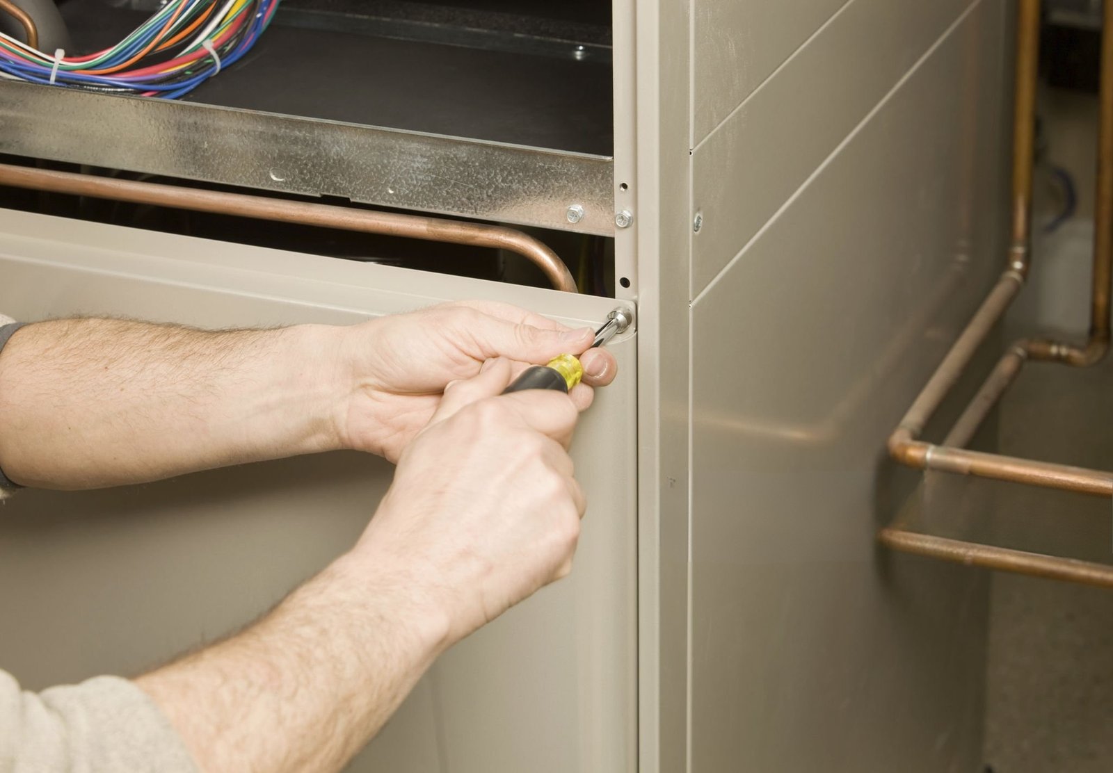 Technician opening a furnace access panel with a screwdriver
